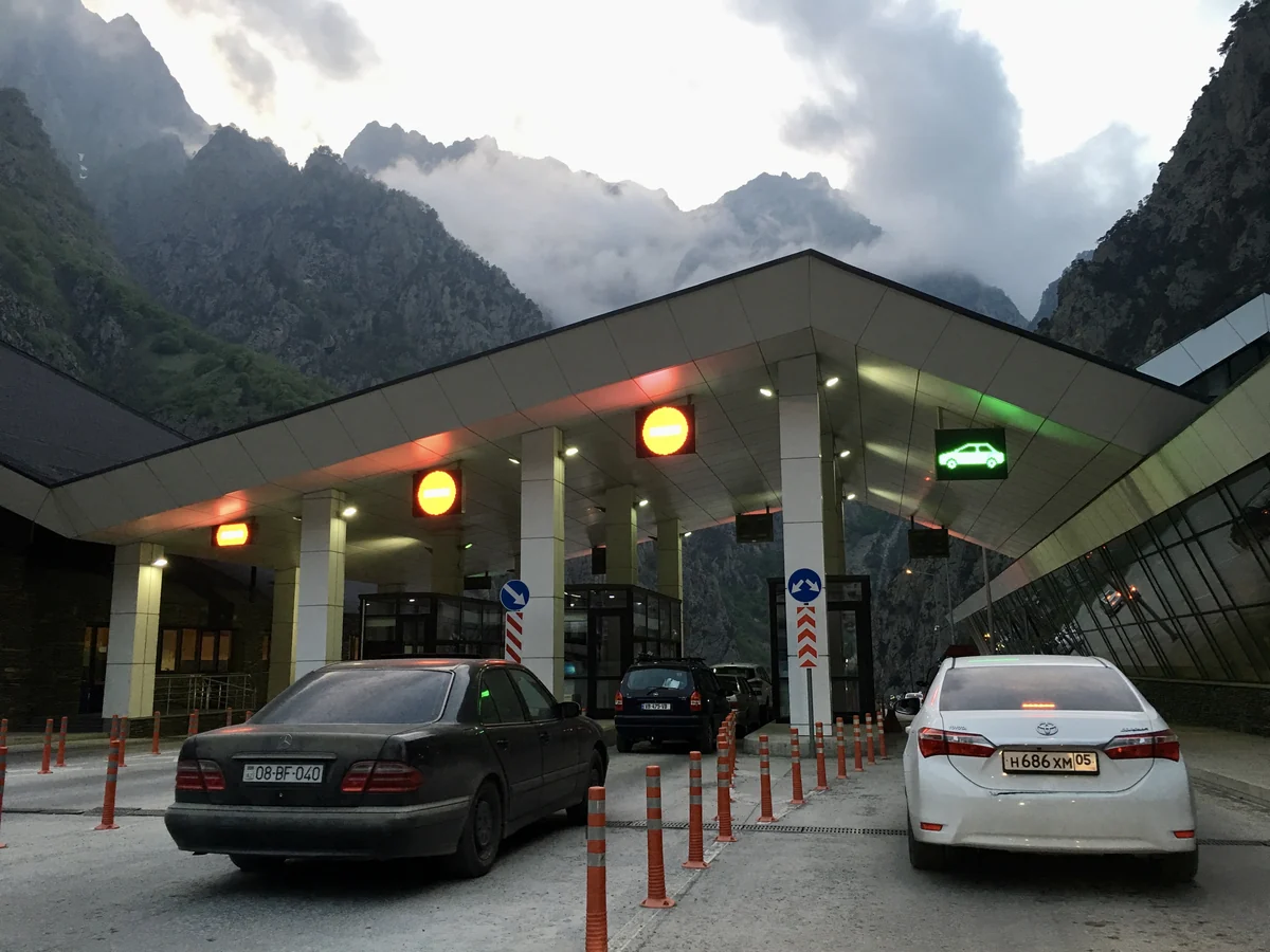 Cars beneath checkpoint lane signs with mountains behind