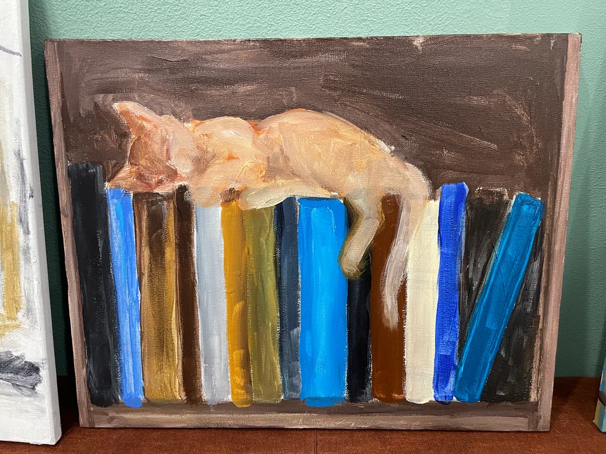 Painting in progress showing a cat resting on books